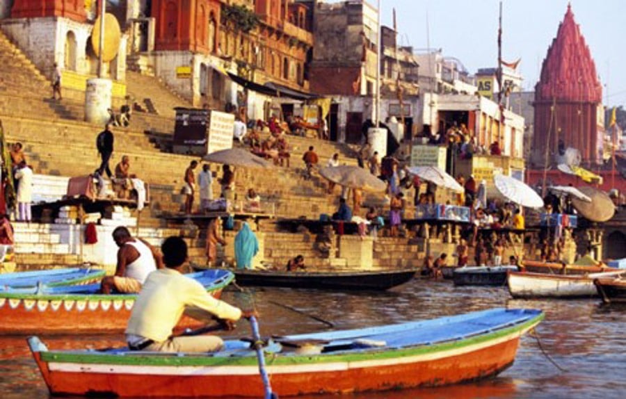 En livlig stad i Indien med en man som seglar en båt, en hög trappa och en vacker röd byggnad