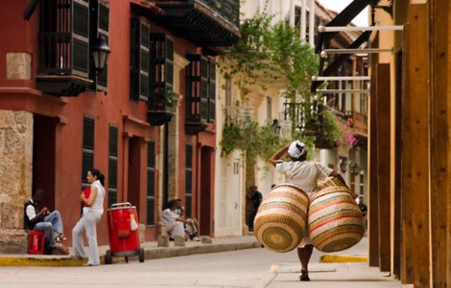 En man bär två stora färgglada korgar på gatorna i Colombia