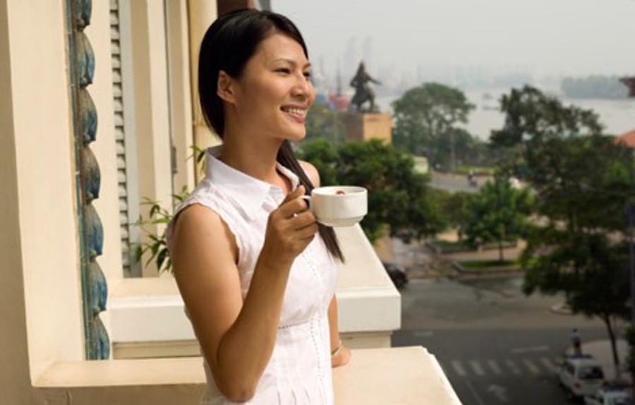 En vietnamesisk kvinna dricker en kopp kaffe från en balkong och njuter av utsikten i Vietnam