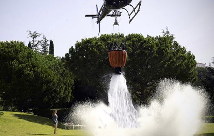 Gevalliahelikopter tappar vatten på ett grönt fält och en kvinna tittar på